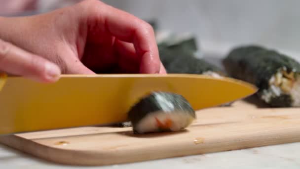 Kokken skærer sushi og ruller lavet af fisk og skaldyr med asiatiske ingredienser med en kniv. Tæt på, makro. Baggrunden er sløret. – Stock-video