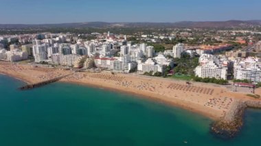 İnsansız hava aracı görüntüleri, Atlantik Okyanusu kıyısında turist kasabası Quareira 'yı çekiyor, turistlerle dolu plajlar. Portekiz, Algarve.