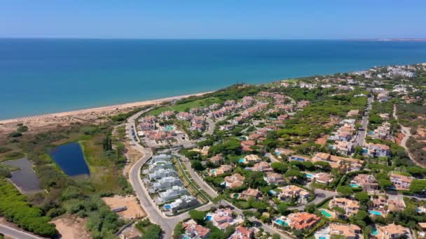 Panorâmica aérea dos edifícios balneários da Quinta do Lago em Vale de Lobo, Algarve, Portugal, Europa. Tiro de telhados de casas de luxo em paisagem verde com montanhas no fundo. Campos de golfe. — Vídeo de Stock