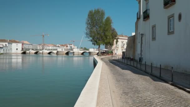 고대 포르투갈의 역사적 인 마을인 타비라 는 자갈 위에 있는 길로 강을 따라 아랍의 다리를 따라 걷고 있다. 안전 장치를 사용하여 촬영. — 비디오