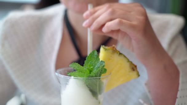 Medelålders kaukasiska kvinna på semester avslappnad dricker en frukt kokos cocktail med mynta blad genom ett sugrör och en skiva ananas. Närbild. — Stockvideo