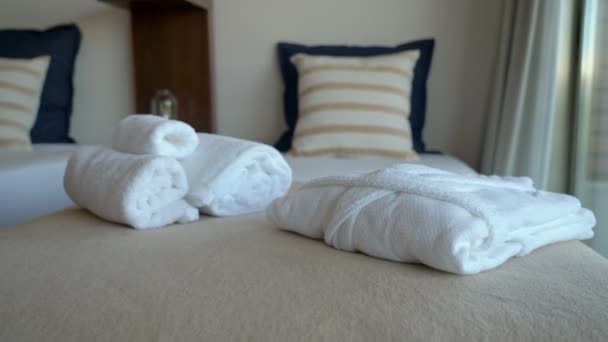Videofelvétel a hotel modern hálószoba szoba ágy és párnák. És fehér törölközők és egy köntös a szálló látogatóinak. — Stock videók