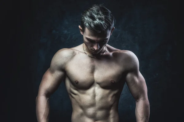 Jovem atleta masculino fisiculturista esteticista posando contra um fundo escuro. Estilo de vida saudável e conceito de esportes. — Fotografia de Stock