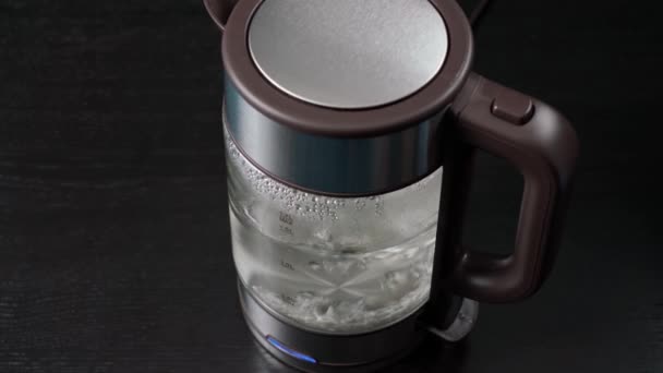 La mano toma un hervidor eléctrico de vidrio para hervir agua, para bebidas, té o café. Sobre un fondo negro. — Vídeos de Stock