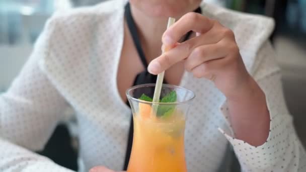 Mulher caucasiana de meia-idade em férias relaxado bebe um coquetel de frutas laranja com folhas de hortelã através de uma palha. Close-up. — Vídeo de Stock