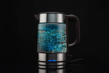 Kaynayan su için elektrikli cam çaydanlık. Sıcak içecekler için. Siyah arka planda köpüklü su..