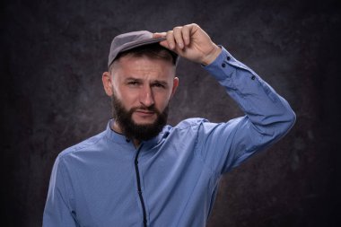 Genç sakallı Avrupalı adam, şık bir şapkanın güneşliğini takınca ciddi duygular gösteriyor. Koyu bir arkaplanda portre
