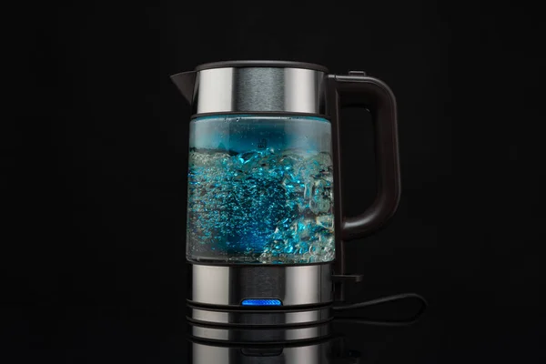 Electric glass kettle for boiling water for hot drinks on a black background with bubbling water.