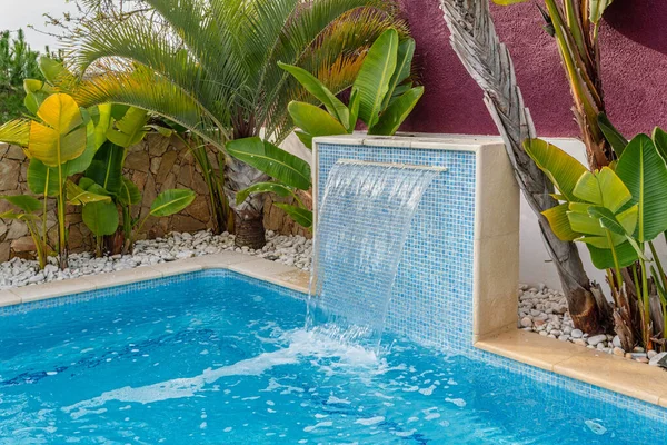 Close-up of a fountain waterfall in a luxury pool near the hotel with palm trees for tourists. — Stockfoto