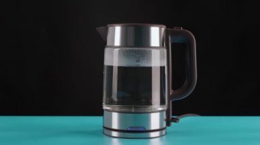 El, kaynar su, içecek, çay ya da kahve için bir bardak elektrikli su ısıtıcısı alır. Siyah bir arkaplanda.