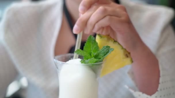 Femme caucasienne d'âge moyen en vacances boissons détendues un cocktail de fruits de noix de coco avec des feuilles de menthe à travers une paille et une tranche d'ananas. Gros plan. — Video