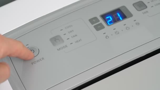 A pessoa pressiona o botão iniciar com o dedo em um condicionador de ar móvel para aquecer e resfriar o quarto no inverno. As lâminas sobem. Close-up. — Vídeo de Stock