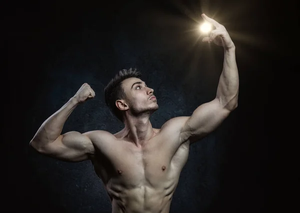 Jeune athlète masculin esthéticien bodybuilder posant sur un fond sombre avec la lumière du soleil dans la main. Style de vie sain et concept sportif. — Photo