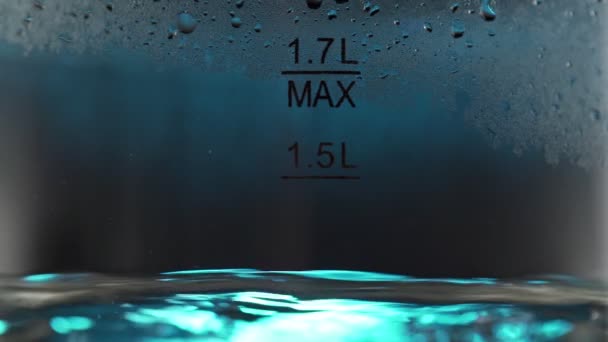 Burbujas borrosas en agua caliente hirviendo dentro de una tetera de vidrio bajo luz azul. Primer plano en macro cámara lenta — Vídeo de stock