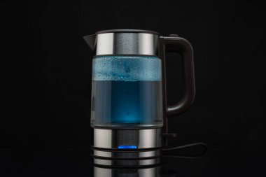 Kaynayan su için elektrikli cam çaydanlık. Sıcak içecekler için. Siyah bir arka planda..