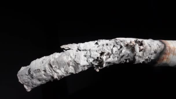 Smoke from a lit cigarette and a drop of ash Close-up on a black background in close-up. Smoking is hazardous to health — Vídeo de stock
