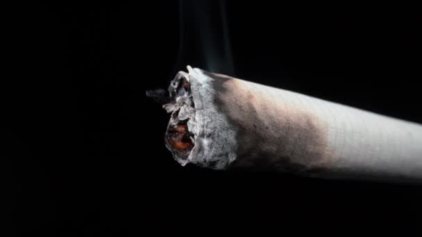 Gyújtás és füst egy égő cigaretta és hamu közelkép egy fekete háttér. A dohányzás káros az egészségre. — Stock videók