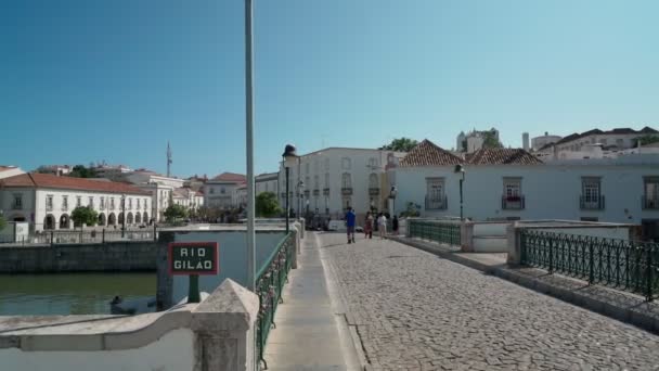 고대 포르투갈의 역사적 인 마을인 타비라 는 자갈 위에 있는 길로 강을 따라 아랍의 다리를 따라 걷고 있다. 안전 장치를 사용하여 촬영. — 비디오