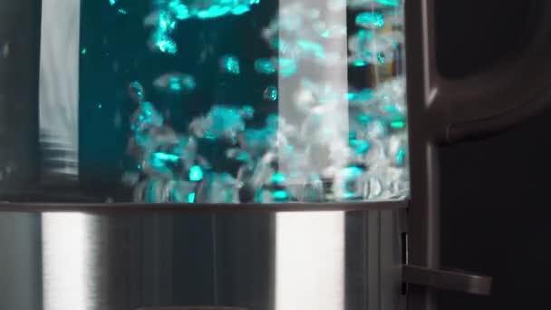 玻璃电水壶中沸腾的水以慢动作起泡.蓝色背光在黑色背景上. — 图库视频影像