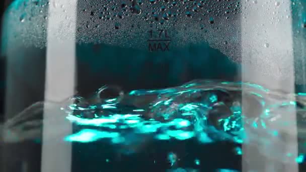 Kokend water in een glazen waterkoker stijgt in slow motion in bellen op. Met blauwe achtergrondverlichting op een zwarte achtergrond. — Stockvideo