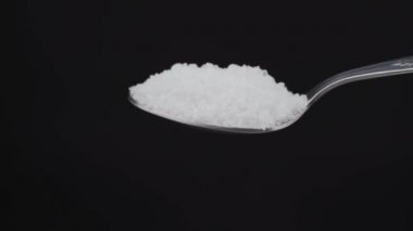 Siyah bir arka plan üzerine demir bir yemek kaşığından deniz tuzu dökmek. Yemek pişirmek için. Ağır çekimde.