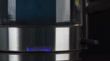 İnsan parmakları su kaynatmak için cam su ısıtıcısının düğmesine basar. Mavi ışıkta kabarcıklar yükseliyor. düşük hareket.