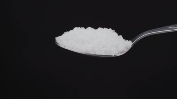 Pouring sea salt from an iron tablespoon on a black background close-up. For cooking food. In slow motion. — Stockvideo