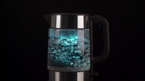 Vařící voda ve skleněné varné konvici stoupá v bublinách zpomaleným pohybem. S modrým podsvícením na černém pozadí. — Stock video