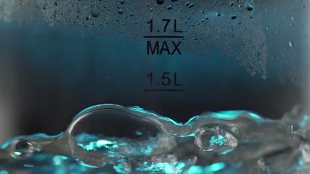 Suddiga bubblor i varmt vatten kokar inuti en tekanna av glas under blått ljus. Närbild i makro slow motion — Stockvideo
