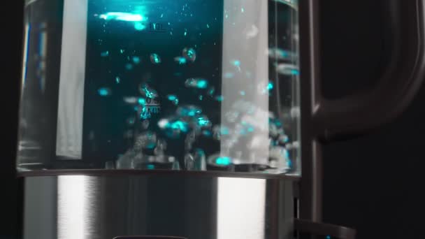 Kokend water in een glazen waterkoker stijgt in slow motion in bellen op. Met blauwe achtergrondverlichting op een zwarte achtergrond. — Stockvideo