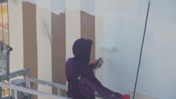 A professional painter on a lift paints the walls of a multi-storey building white. — Vídeo de Stock