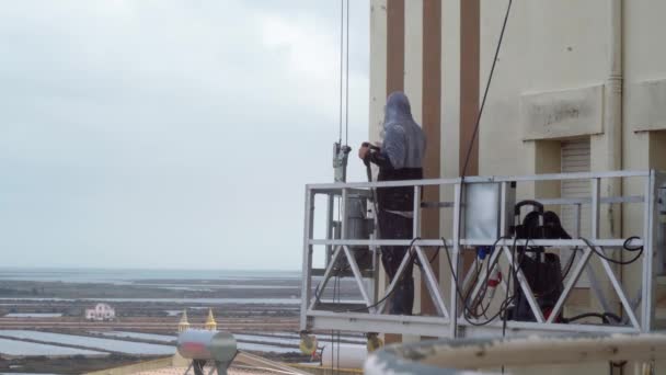 Um homem usa uma máquina de alta pressão para desinfetar as paredes de um edifício de vários andares para reparos subsequentes. Em uma talha de pintura industrial. — Vídeo de Stock