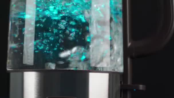 Kokend water in een glazen waterkoker stijgt in slow motion in bellen op. Met blauwe achtergrondverlichting op een zwarte achtergrond. — Stockvideo