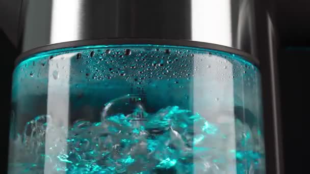 Vařící voda ve skleněné varné konvici stoupá v bublinách zpomaleným pohybem. S modrým podsvícením na černém pozadí. — Stock video