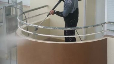 Bir adam çok katlı bir binanın duvarlarını dezenfekte etmek için yüksek basınçlı bir makine kullanıyor. Endüstriyel boya asansöründe.