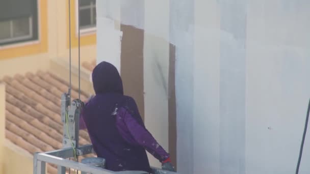 A professional painter on a lift paints the walls of a multi-storey building white. — Stockvideo