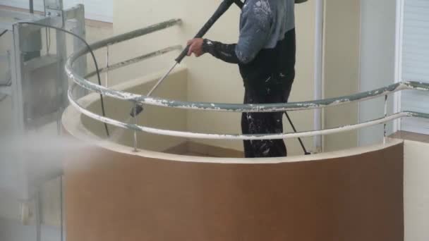 Un homme utilise une machine à haute pression pour désinfecter les murs d'un immeuble de plusieurs étages pour des réparations ultérieures. Sur un palan à peinture industriel. — Video