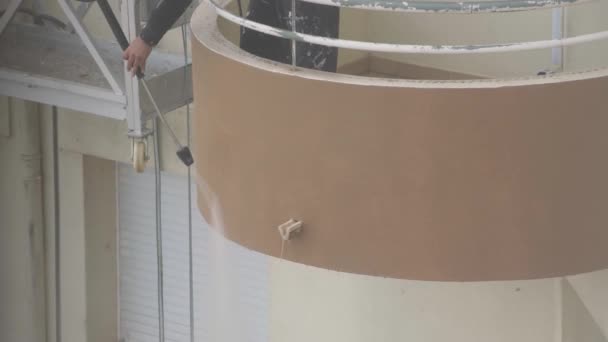 Bir adam çok katlı bir binanın duvarlarını dezenfekte etmek için yüksek basınçlı bir makine kullanıyor. Endüstriyel boya asansöründe. — Stok video