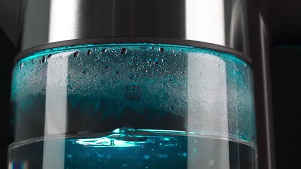 Boiling water in a glass electric kettle rises in bubbles in slow motion. With blue backlighting on a black background cluse up — Vídeo de Stock