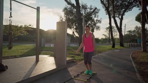 Young caucasian woman in the park practicing rope ladder jumping for endurance and weight loss. In slow motion. Promoting a healthy lifestyle — Stok video