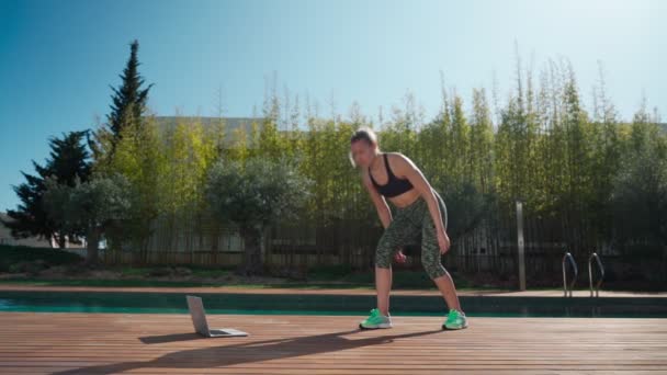 Young caucasian woman in the park practicing jumping with personal trainer online via laptop. During isolation and pandemic. In slow motion. — 图库视频影像