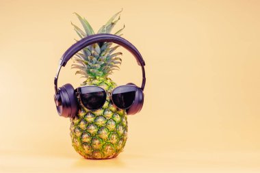 Creative idea of a pineapple image of a person headphones and glasses as a relaxing tourist on vacation. On a yellow background.