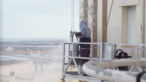 Чоловік використовує машину високого тиску для дезінфекції стін багатоповерхової будівлі для подальшого ремонту. На промисловому підйомнику фарби . — стокове відео