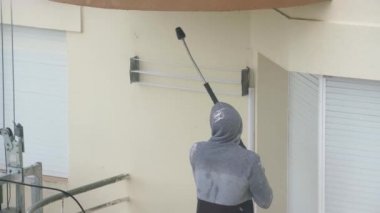 Bir adam çok katlı bir binanın duvarlarını dezenfekte etmek için yüksek basınçlı bir makine kullanıyor. Endüstriyel boya asansöründe.