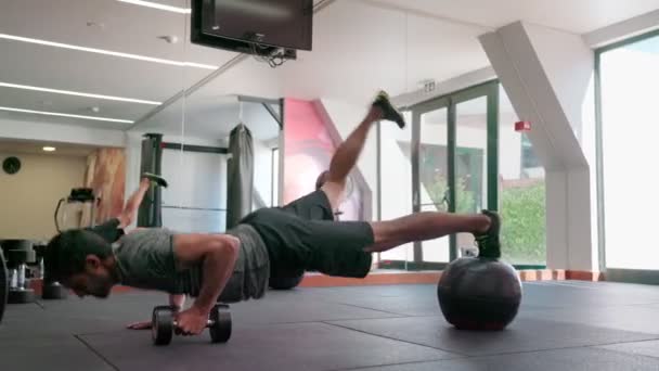 Un hombre de mediana edad realiza ejercicios para la funcionalidad del cuerpo y la resistencia. Push-ups y filas con mancuernas en la bola horizontalmente. En el gimnasio. — Vídeos de Stock
