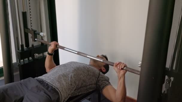 Sportowy biały mężczyzna w średnim wieku trenuje wyciskanie ławki do klatki piersiowej na symulatorze sportowym. aparatura szkoleniowa — Wideo stockowe