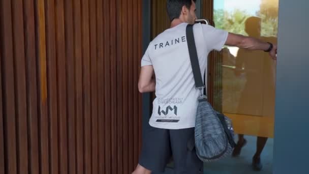 Męski trener fitness wchodzi do prywatnego domu, a kobieta otwiera drzwi do osobistego treningu fitness. Z torbą i łuskami. — Wideo stockowe