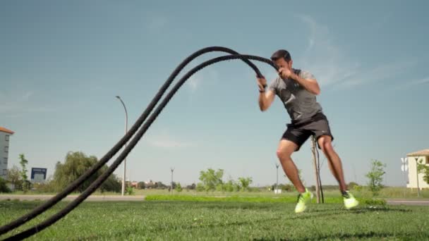 Atleta caucásico muscular hace olas con una cuerda de batalla en la hierba exterior. Un atleta profesional se dedica a las cuerdas al aire libre. mociones lentas — Vídeo de stock