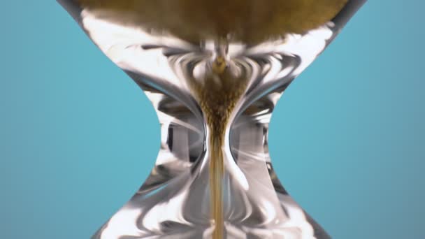 An hourglass made of yellow metal shavings passes through a funnel, symbolizing the concept of time in motion. Macro — Αρχείο Βίντεο