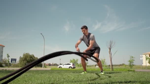Atleta caucasico muscolare fa onde con una corda da battaglia sull'erba fuori. Un atleta professionista è impegnato con corde all'aperto. rallentamenti — Video Stock